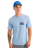 Man wearing a light blue t-shirt with Huk logo and a matching blue cap on a white background