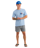 Man wearing a light blue t-shirt with Huk logo and a matching blue cap on a white background