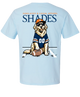 A light blue short-sleeve t-shirt shown from the back, featuring a graphic of a golden retriever wearing a navy and orange football jersey, sunglasses, and an orange cap, sitting next to a football. The word 'SHADES' is printed in large navy letters above the dog, with smaller orange text reading 'SUNGLASSES & CASUAL APPAREL' above that.