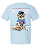 A light blue short-sleeve t-shirt showing the back graphic. The graphic features a cartoon golden retriever wearing a blue and red football jersey, a matching cap, sunglasses, and sitting next to a football.