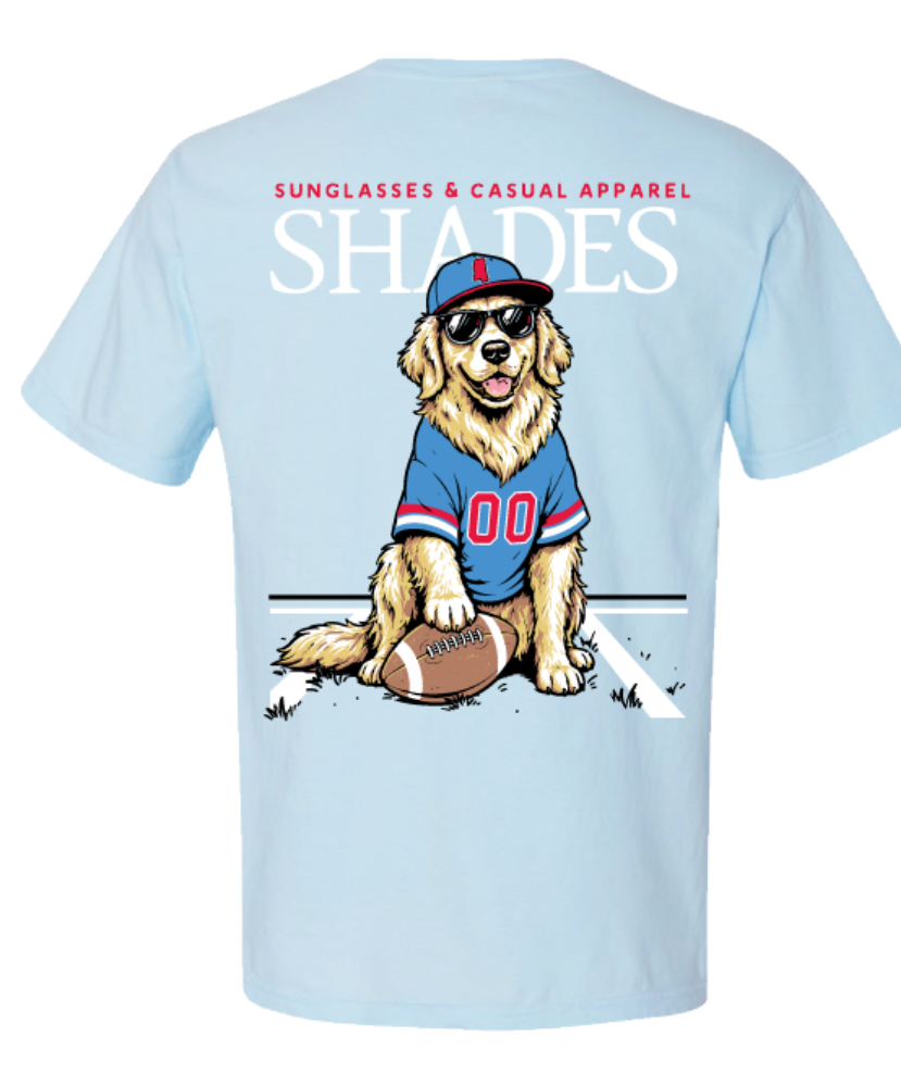 A light blue short-sleeve t-shirt showing the back graphic. The graphic features a cartoon golden retriever wearing a blue and red football jersey, a matching cap, sunglasses, and sitting next to a football.