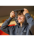 A smiling man wearing a dark gray hoodie with a patterned interior hood lining, holding the hood up with both hands.