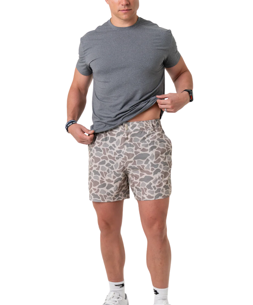 Man wearing a gray t-shirt and camoflage patterned shorts on a white background