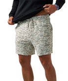 A person wearing patterned shorts and pulling up a black long-sleeve shirt against a plain white background.