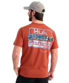 Man wearing an RED Huk Fishing t-shirt with a fishing lure logo on the back against a white background