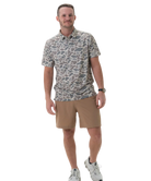 Man wearing a patterned shirt and beige shorts on a white background