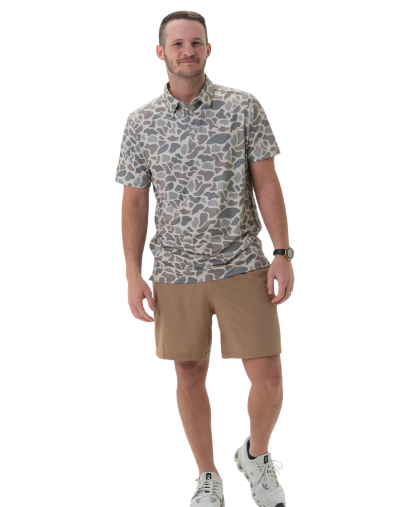 Man wearing a patterned shirt and beige shorts on a white background