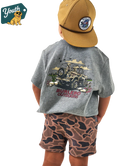 Child wearing a gray t-shirt with a JEEP graphic design and camouflage shorts, standing against a white background.