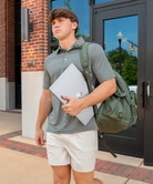 Young man with a backpack and folder walking outside a building