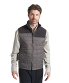 Man wearing a gray quilted vest over a light shirt on a white background