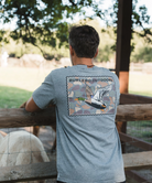 Man wearing a gray t-shirt with a mallard duck graphic and 'Burlebo Outdoors' text, standing outdoors.