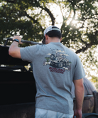 Man wearing a gray t-shirt with a bronco Burlebo graphic design and text, standing outdoors with trees in the background.