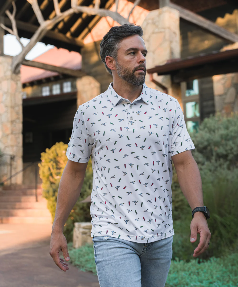 Man wearing a white polo shirt with small colorful ducks and shotgun shells patterns on a white background