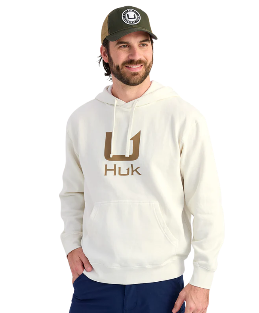 Man wearing a cream hoodie with 'Huk' logo and a cap on a white background
