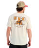 Man wearing a cream t-shirt with a dog graphic and 'HUK' branding on a white background