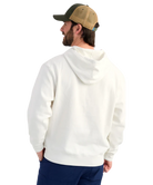 Man wearing a cream hoodie with 'Huk' logo and a cap on a white background