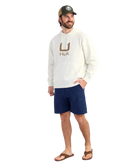 Man wearing a cream hoodie with 'Huk' logo and a cap on a white background