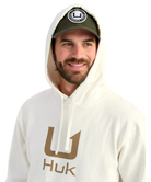 Man wearing a cream hoodie with 'Huk' logo and a cap on a white background