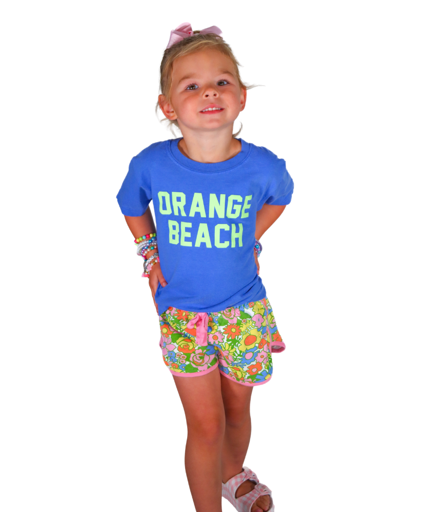 Young girl wearing a blue shirt with 'Orange Beach' text and floral shorts on a white background