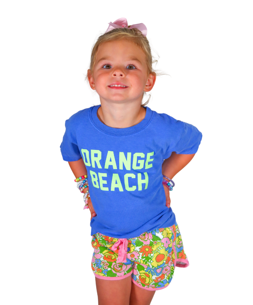 Young girl wearing a blue 'Orange Beach' shirt and colorful shorts on a white background