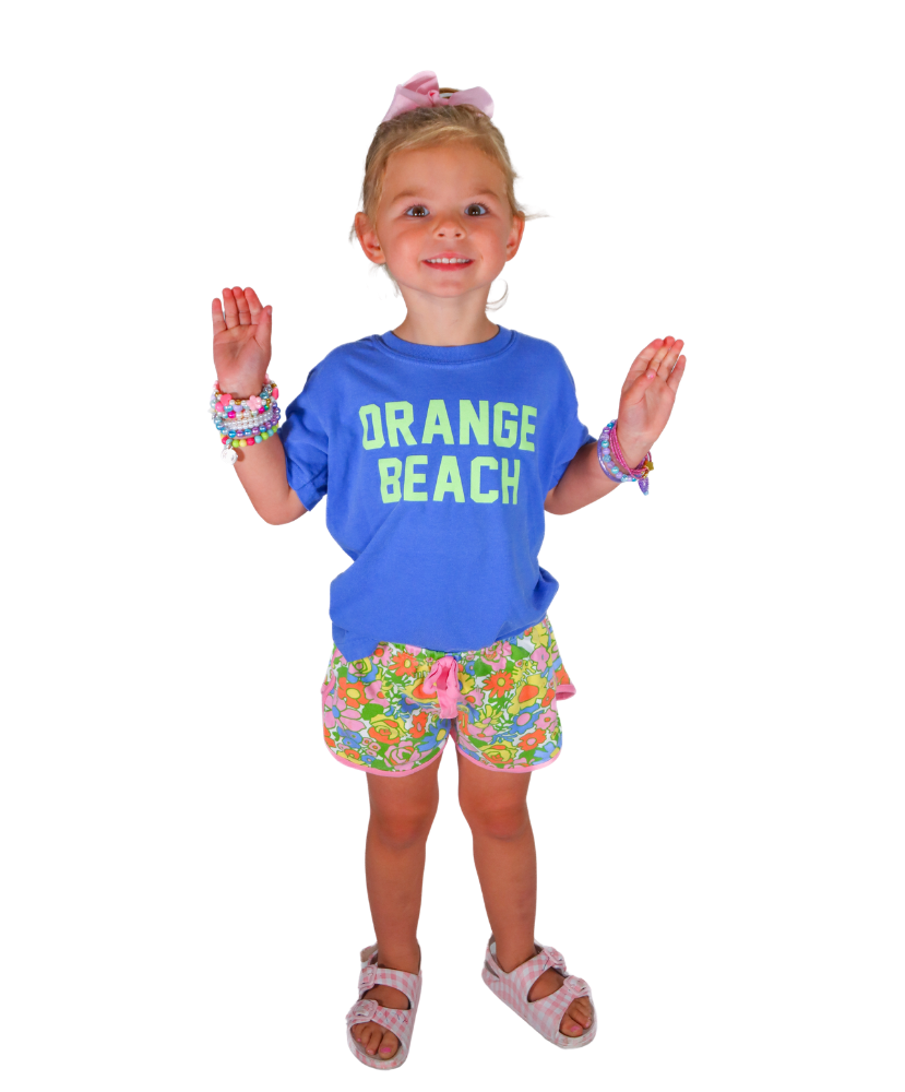 Young girl wearing a blue 'Orange Beach' shirt and floral shorts on a white background
