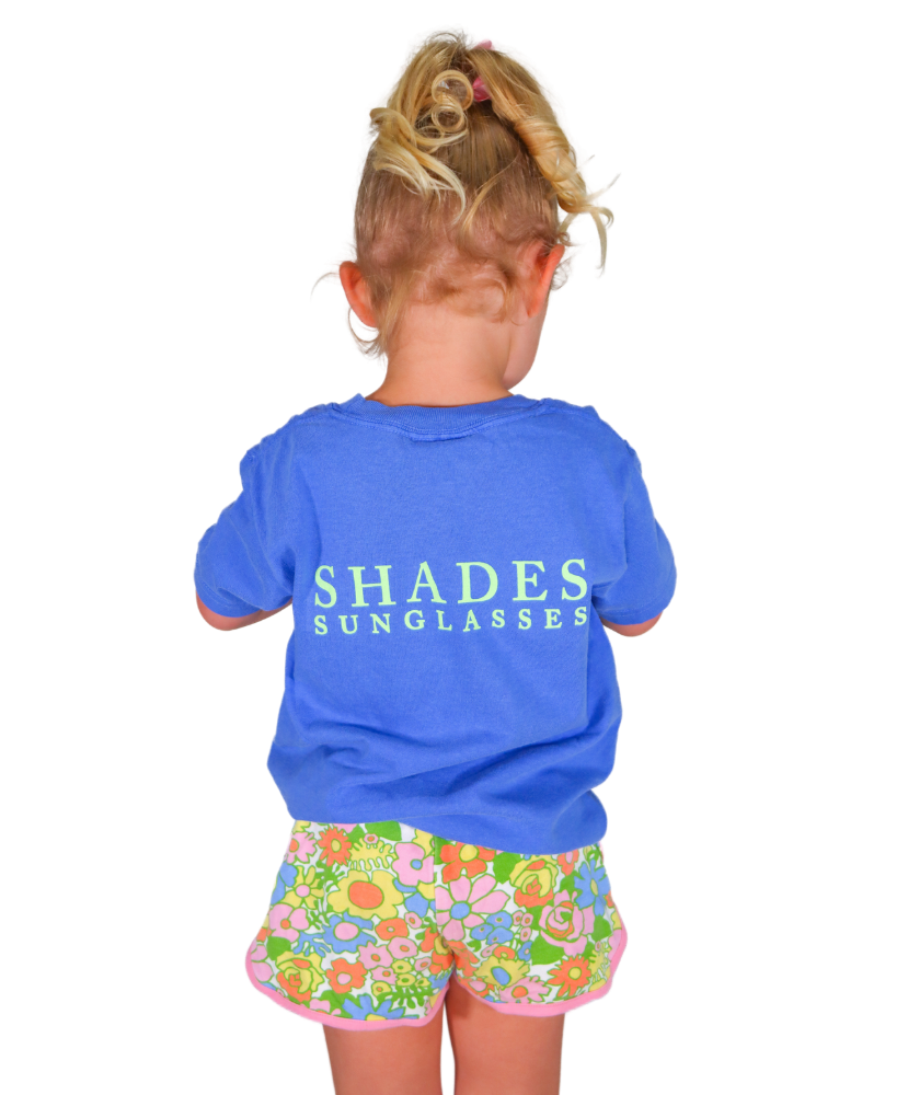 Child wearing a blue shirt with 'SHADES SUNGLASSES' text and colorful shorts on a white background