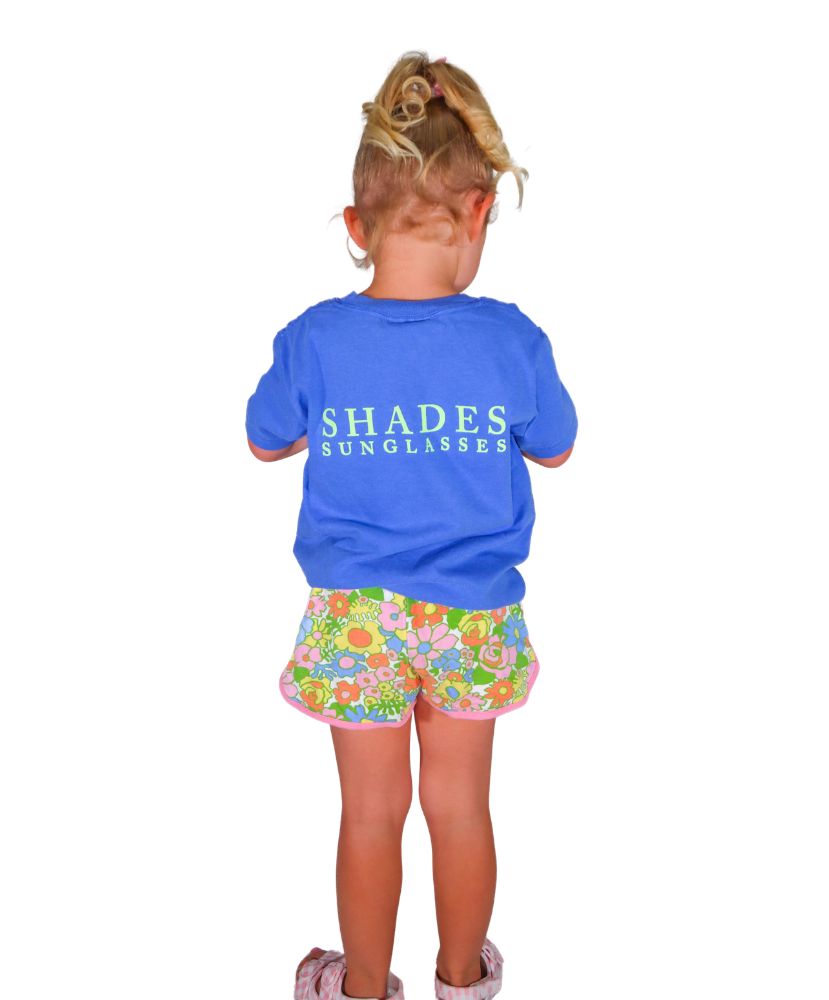 Child wearing a blue shirt with 'SHADES SUNGLASSES' text and floral shorts on a white background