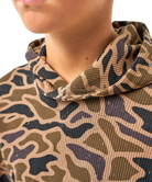 Close-up of a person wearing a textured hooded sweatshirt with a camouflage pattern in tan, olive green, and dark charcoal gray.