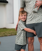 Child and adult wearing matching flying duck patterned shirts and shorts outdoors.