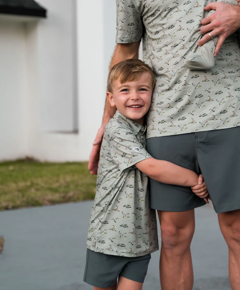 Child and adult wearing matching flying duck patterned shirts and shorts outdoors.