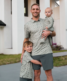 Man holding two children outdoors in front of a house