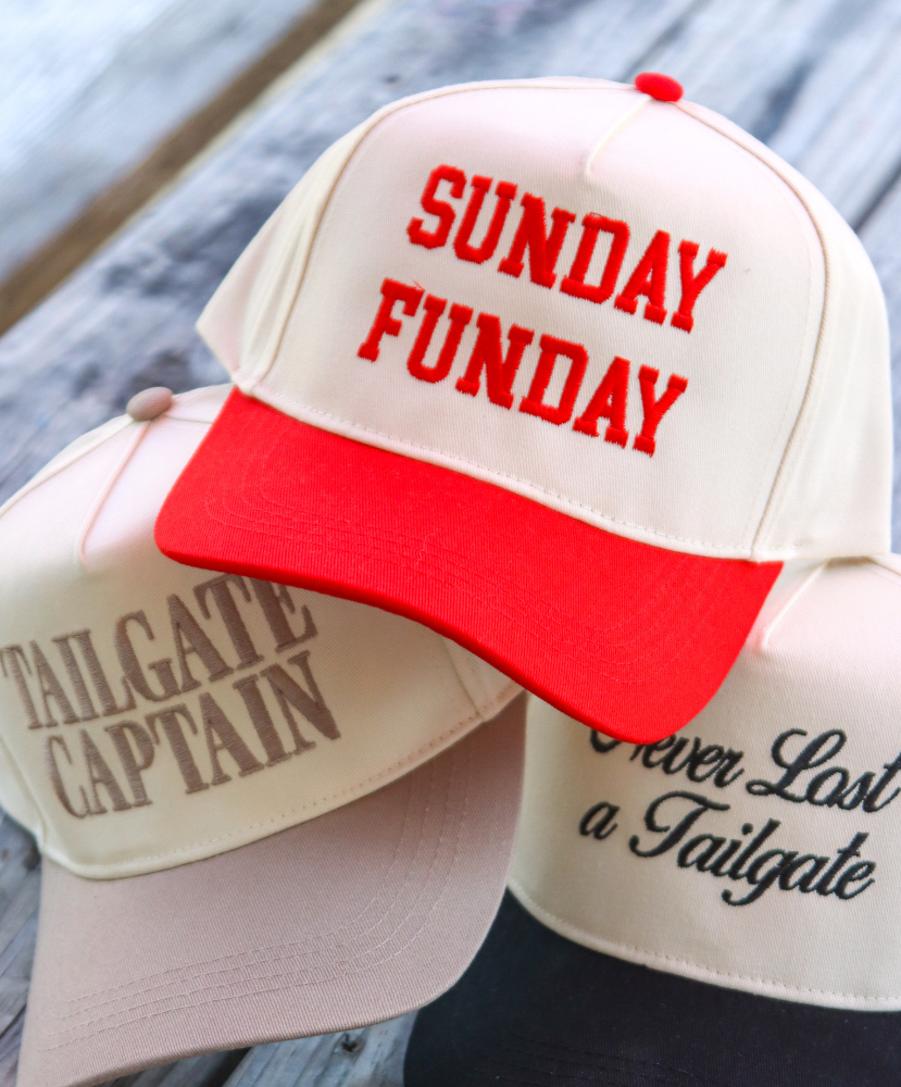 Two baseball caps with text 'SUNDAY FUNDAY' and 'TAILGATE CAPTAIN' on a wooden surface.