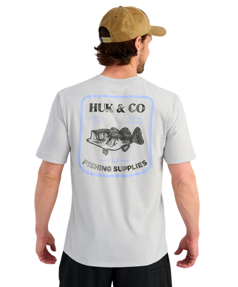 Man wearing a gray t-shirt with Huk & Co fishing supplies logo on the back, Bass graphic, standing against a white background.