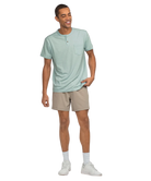 Man wearing a light green henley shirt and beige shorts on a white background