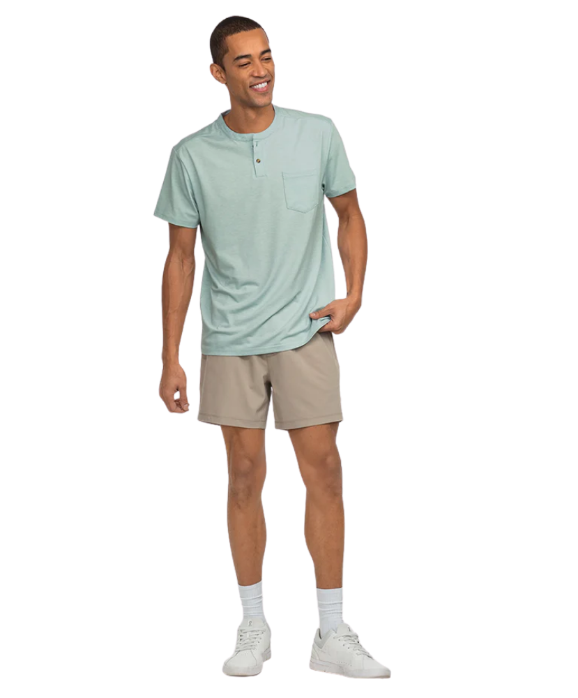 Man wearing a light green henley shirt and beige shorts on a white background