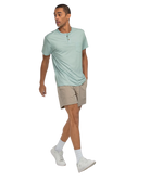 Man wearing a light green henley t-shirt and beige shorts on a white background
