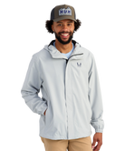 Man wearing a light gray HUK jacket and cap with a logo on a white background