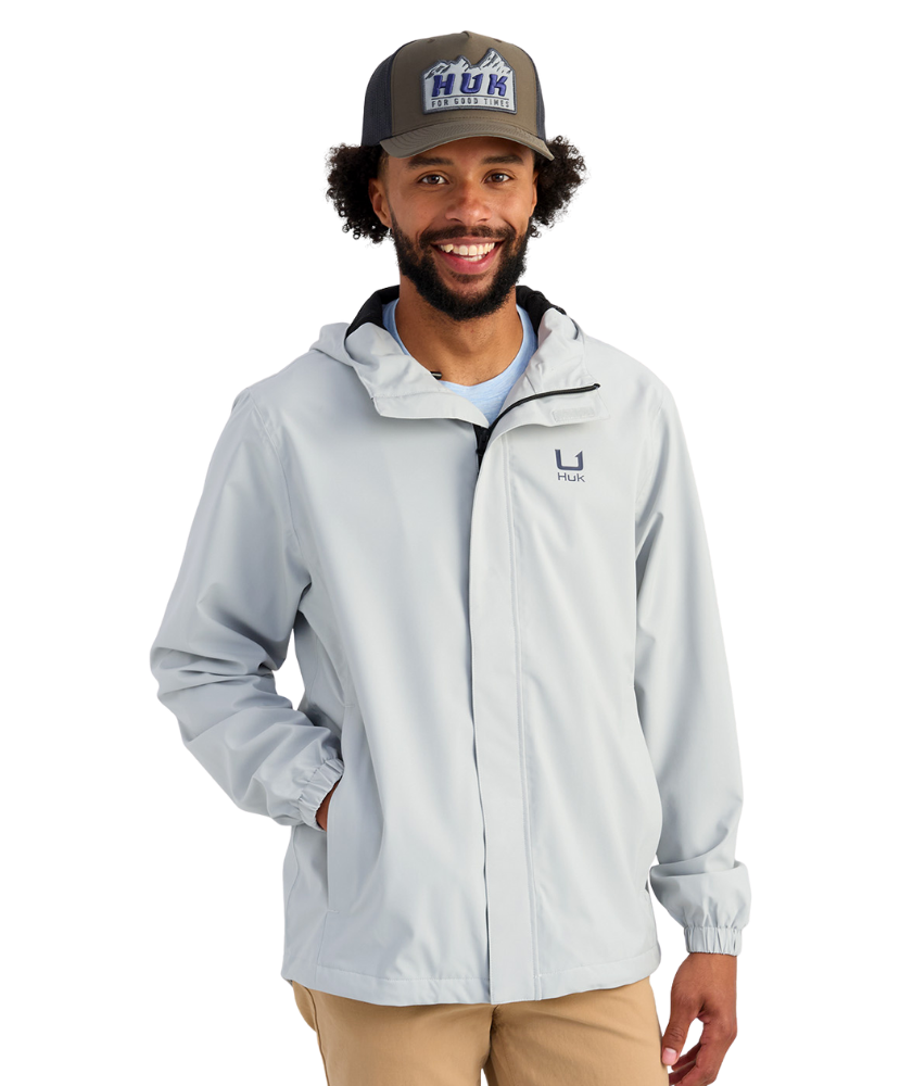Man wearing a light gray HUK jacket and cap with a logo on a white background
