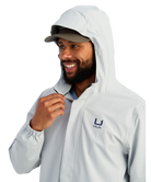 Man wearing a light gray HUK jacket and cap with a logo on a white background