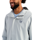 Man wearing a light gray HUK jacket and cap with a logo on a white background