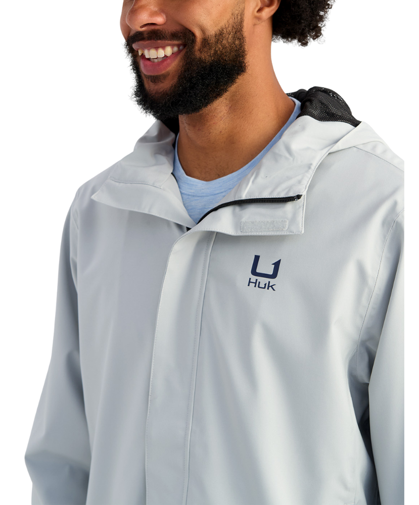 Man wearing a light gray HUK jacket and cap with a logo on a white background