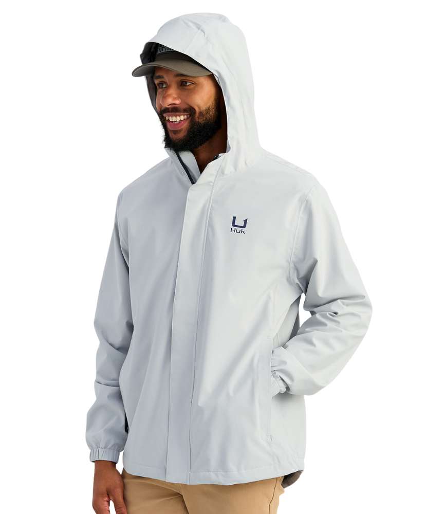 Man wearing a light gray HUK jacket and cap with a logo on a white background