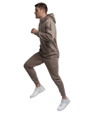 Man wearing a brown hoodie and joggers and white sneakers on a white background