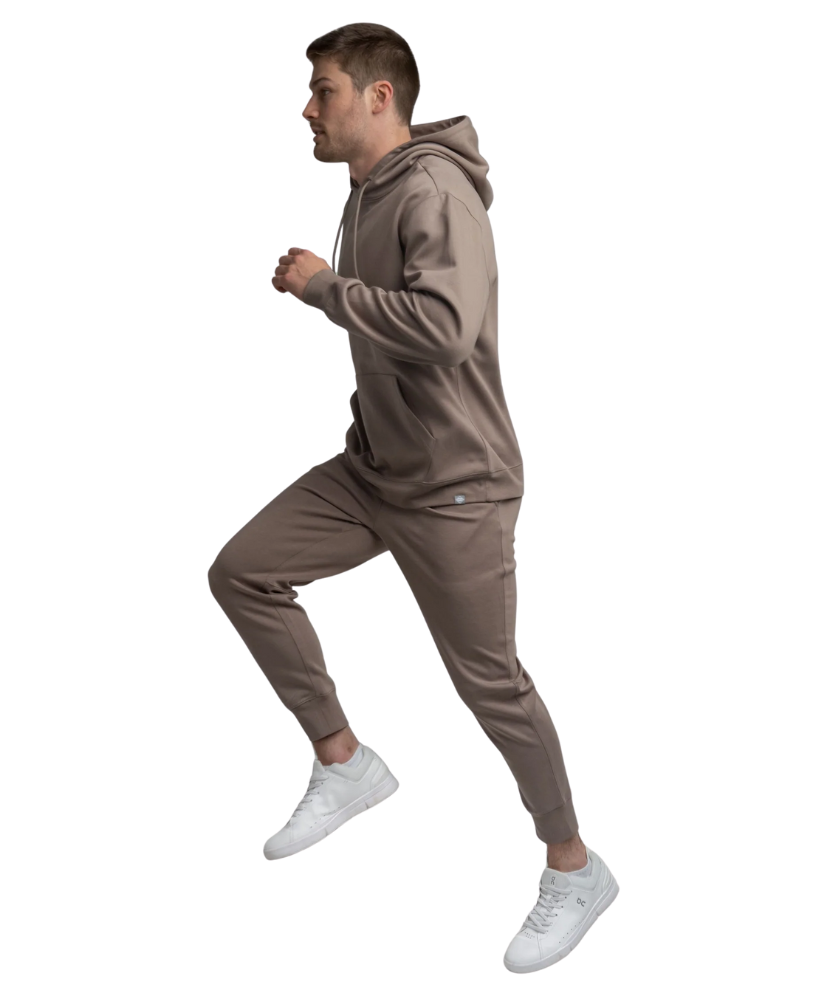 Man wearing a brown hoodie and joggers and white sneakers on a white background
