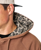 Close-up of a person wearing a brown hoodie with a camouflage hood lining on a white background
