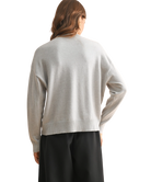 Person wearing a light gray sweater and black pants on a white background