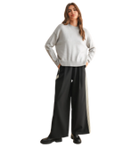 Woman wearing a white sweater and black pants with a stripe on a white background