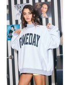 Woman wearing a heather grey sweatshirt with 'GAMEDAY' printed on it against a white background