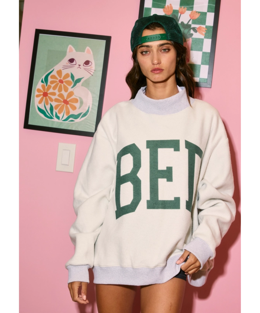 Person wearing a white sweatshirt with green text in a room with pink walls and decorative elements.
