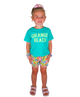 Young girl wearing a turquoise 'Orange Beach' shirt and colorful shorts on a white background